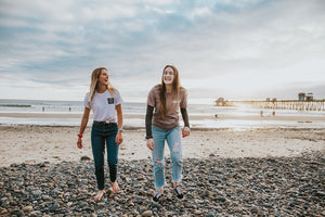 Two young women on the beach wearing colorful sunscreen on their noses and laughing